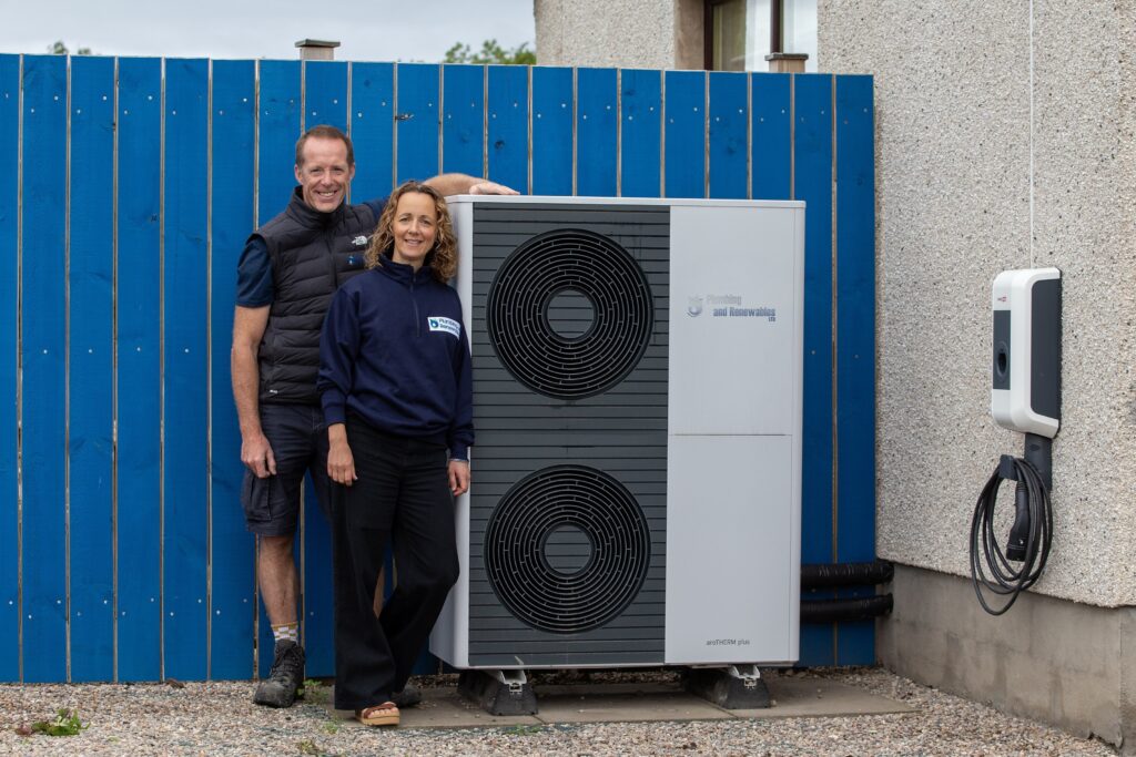 Two people stand next to heat pump