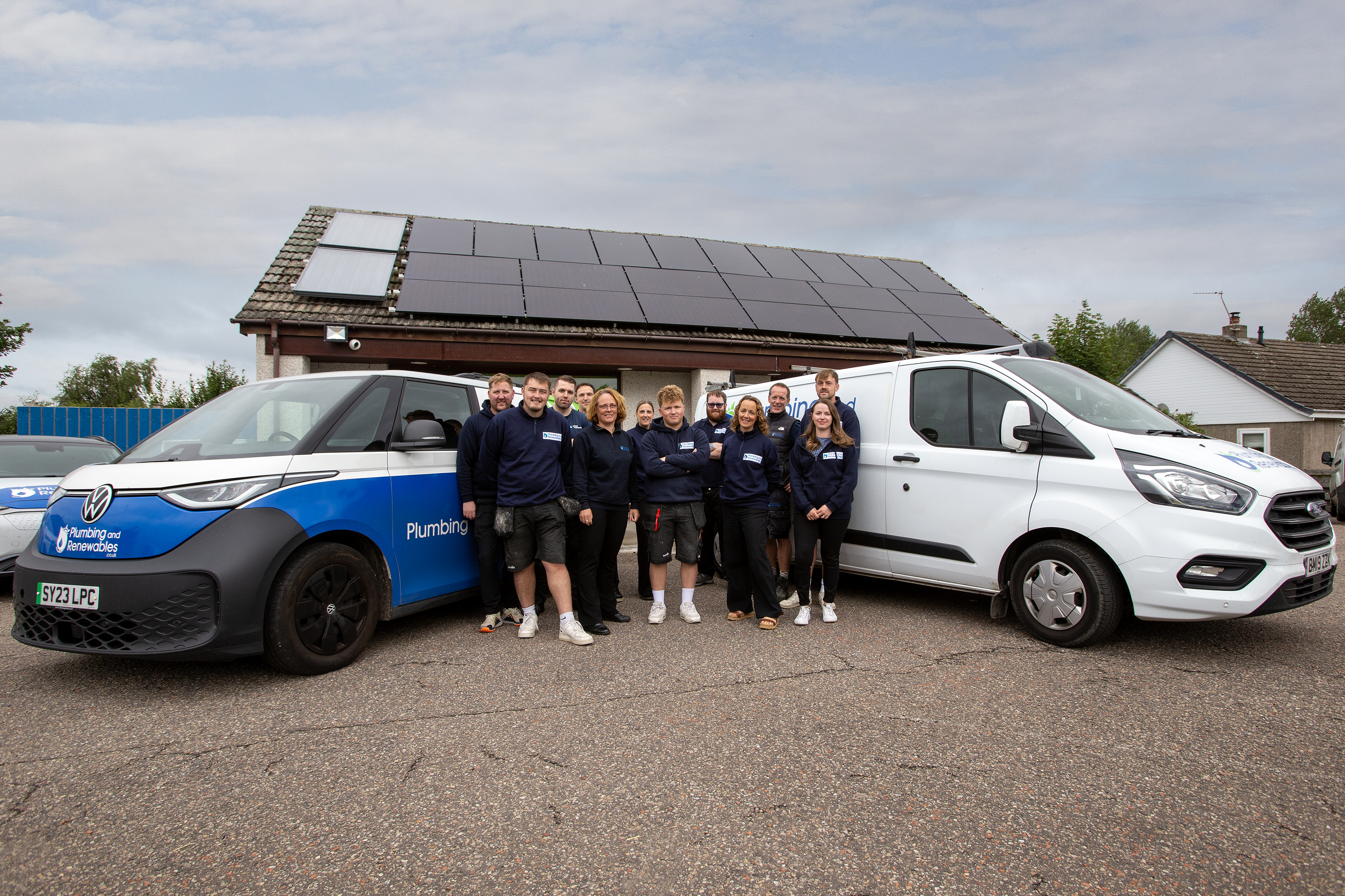 A team of workers stands between two branded vans outside a building with solar panels on the roof.
